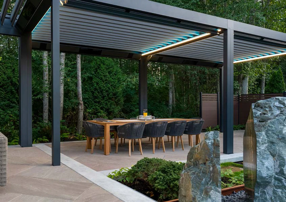 Pérgola Algarve de color gris oscuro, independiente, con lamas orientables, luz integrada y marquesina.