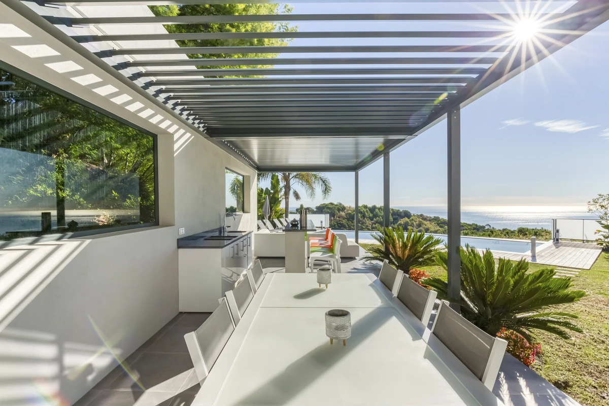 Pérgola Camargue de Renson adosada a villa con vista al mar, lamas orientables y diseño moderno para confort al aire libre.